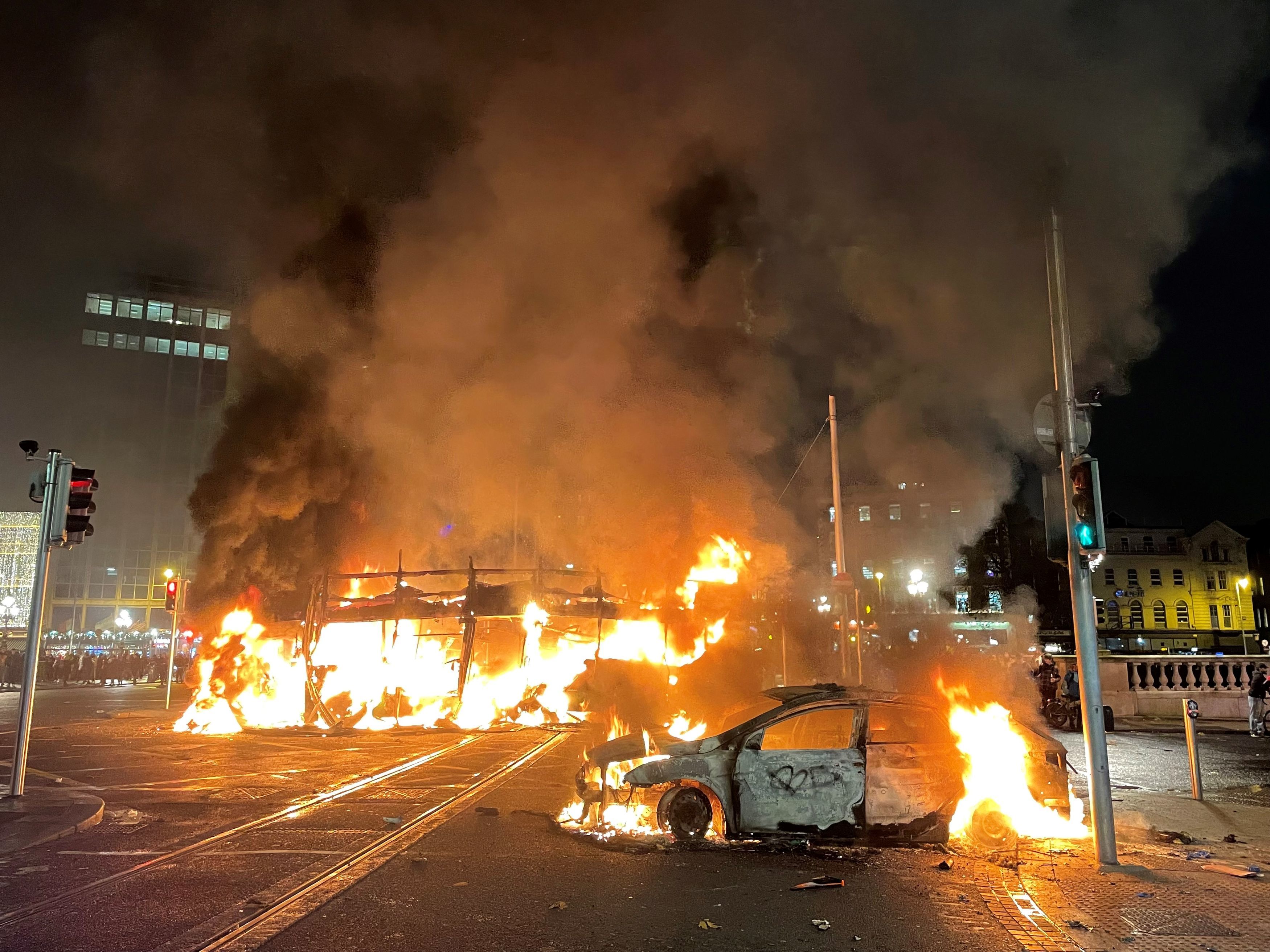 <p>A bus and car on fire in Dublin’s city centre after violent protests erupted following a stabbing attack</p>