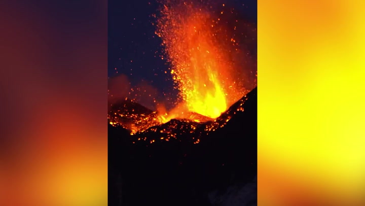 Mount Etna emits molten lava and releases smoke into the dark sky at night.