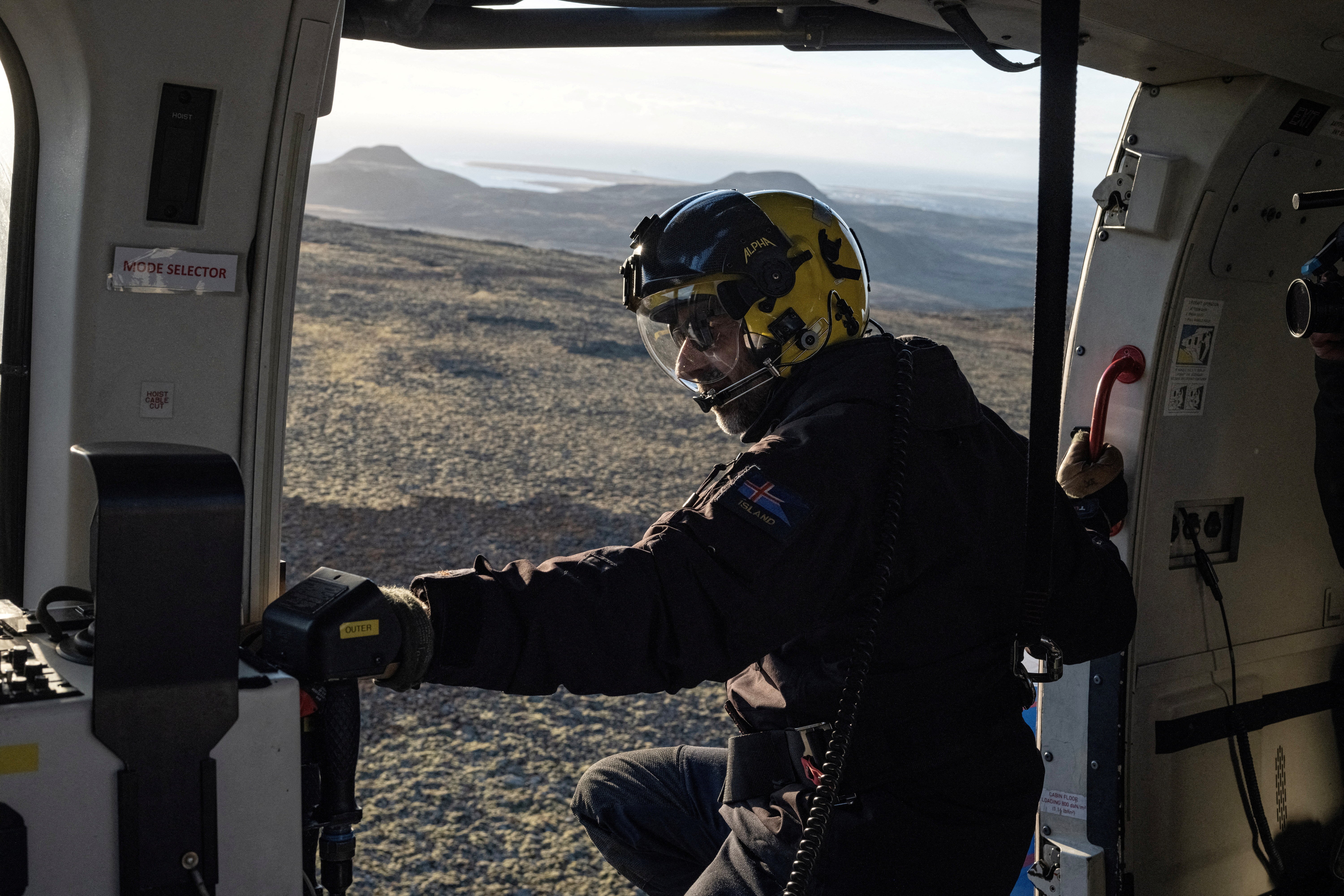 <p>A member of the Coast Guard flies in a helicopter near the evacuated town of Grindavik, in Iceland</p>