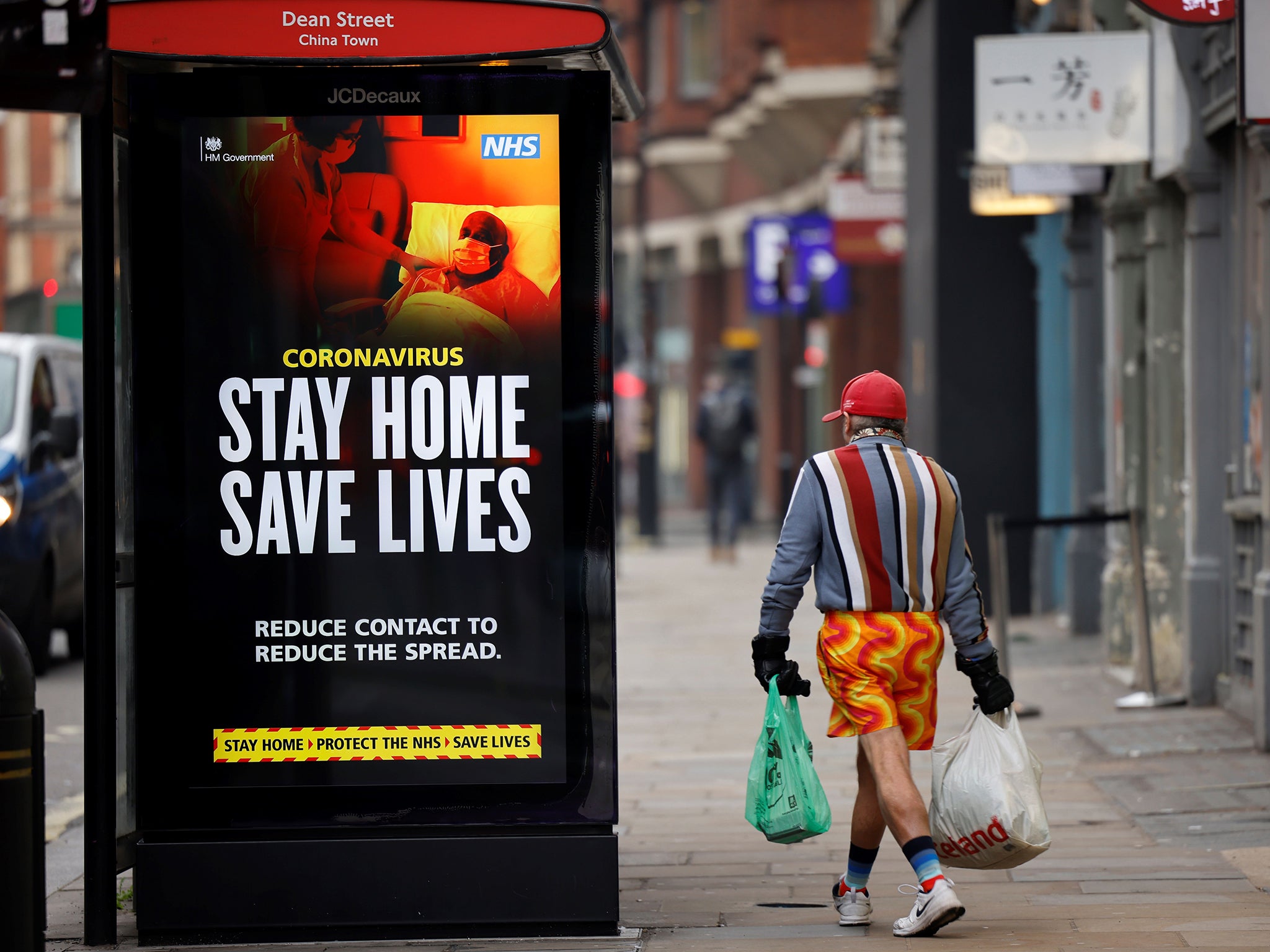 <p>A shopper walks past NHS signage promoting ’Stay Home, Save Lives’ on a bus shelter in central London in January 2021</p>