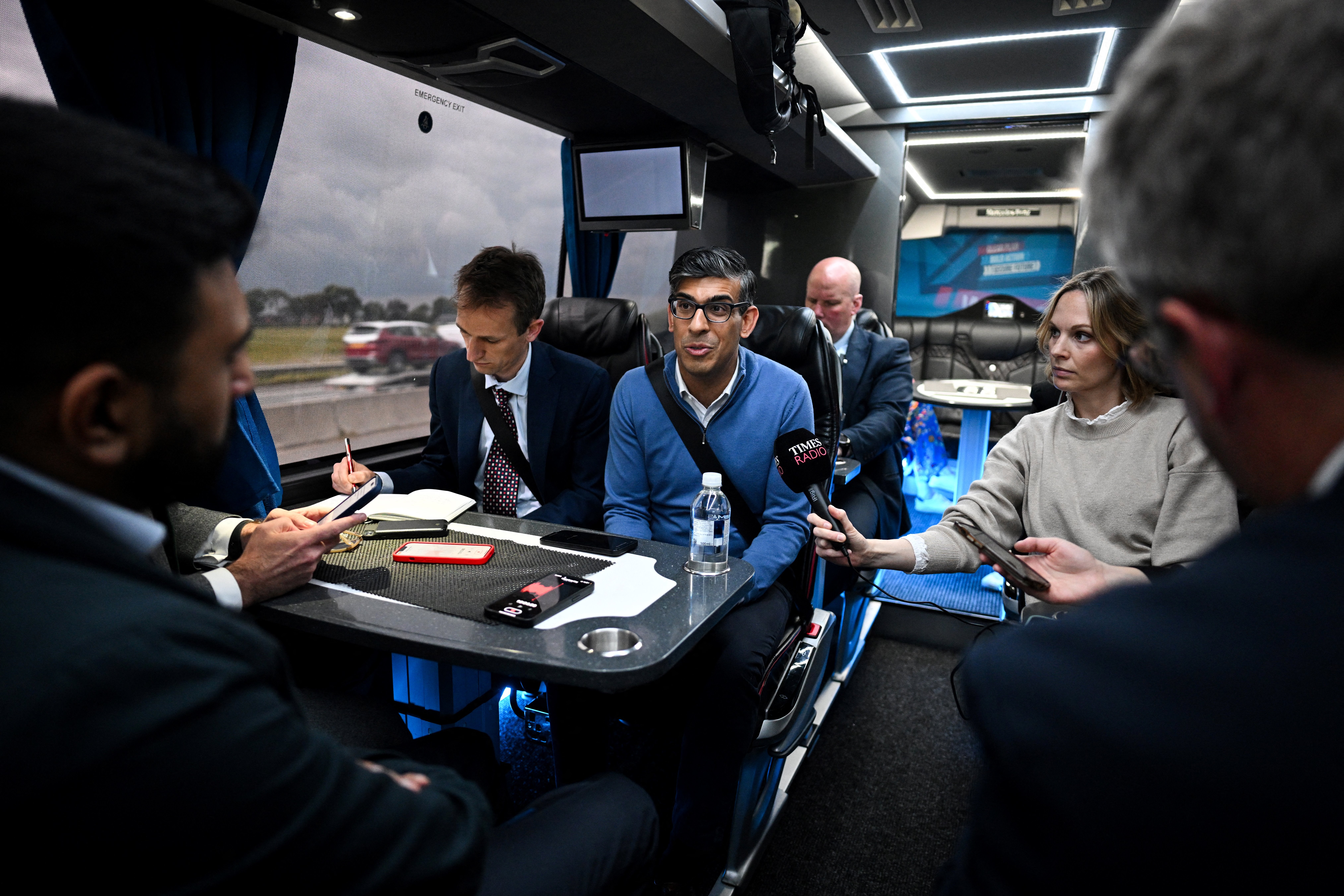 Rishi Sunak (C) speaks with journalists aboard of the party campaign bus on its way to Grimsby after leaving Doncaster Station, on the M180