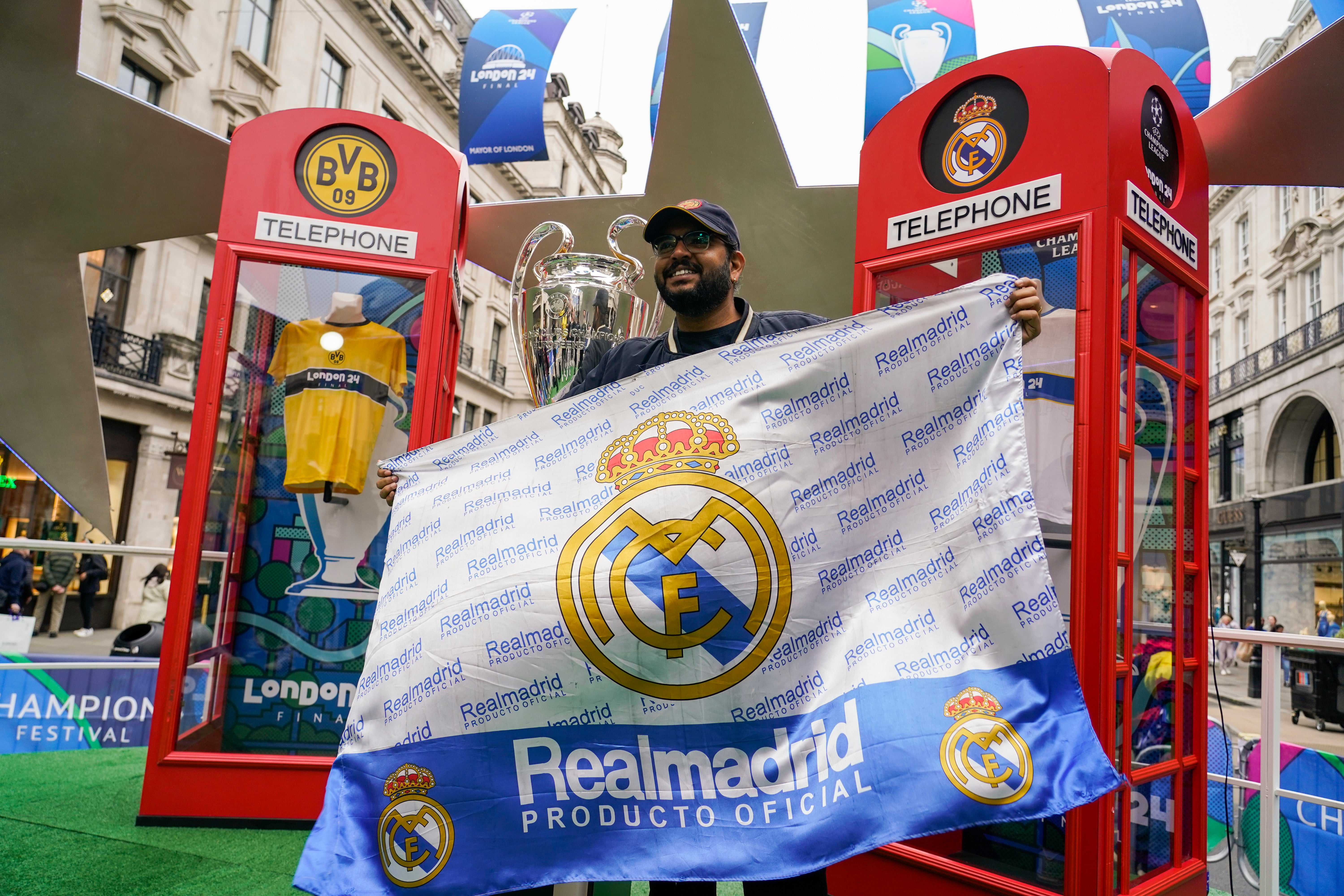 A fan displays a Real Madrid flag as he poses next to the trophy in a fan zone in Regent Street