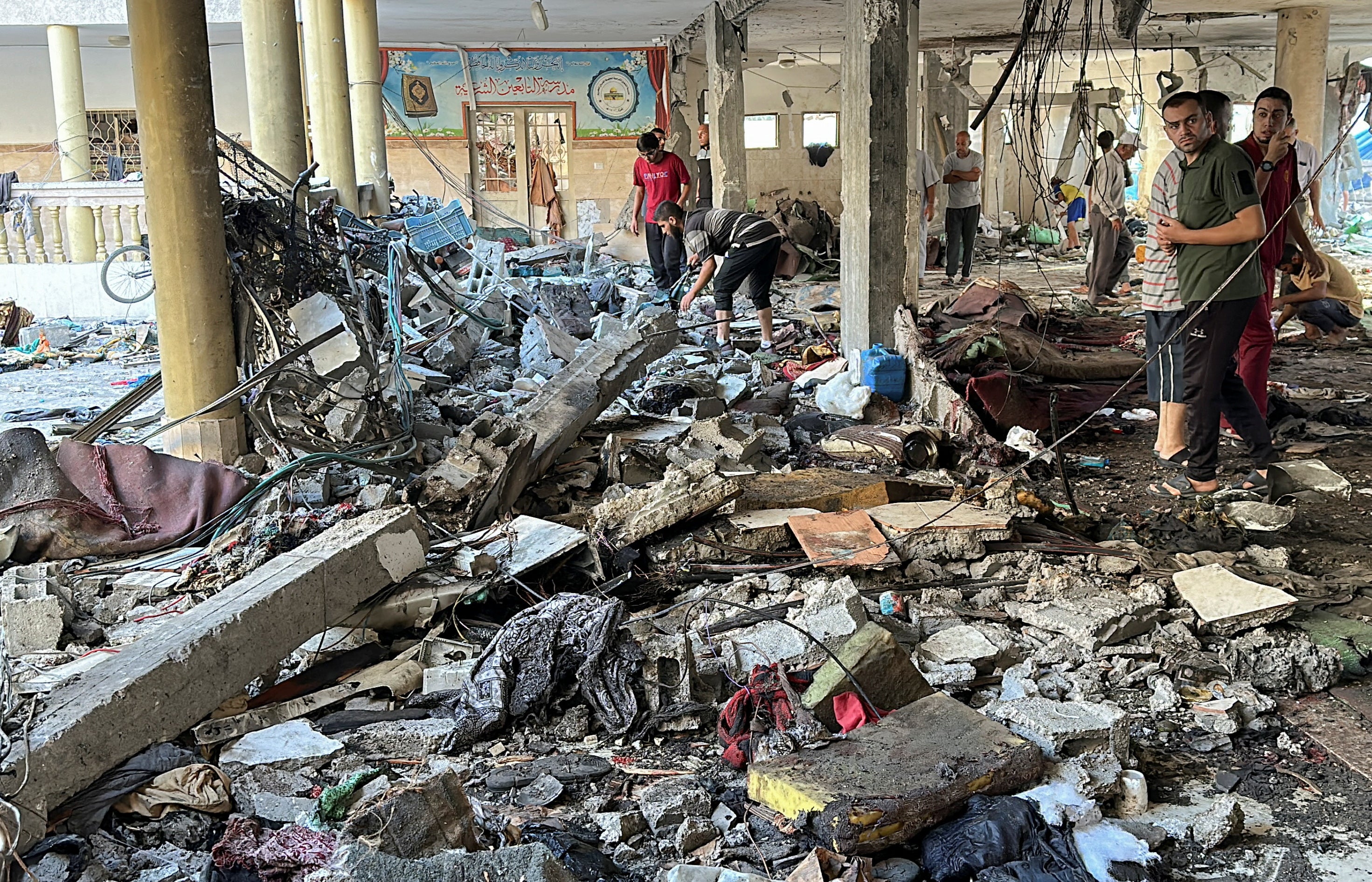 Palestinians inspect the site of an Israeli strike on a school sheltering displaced people