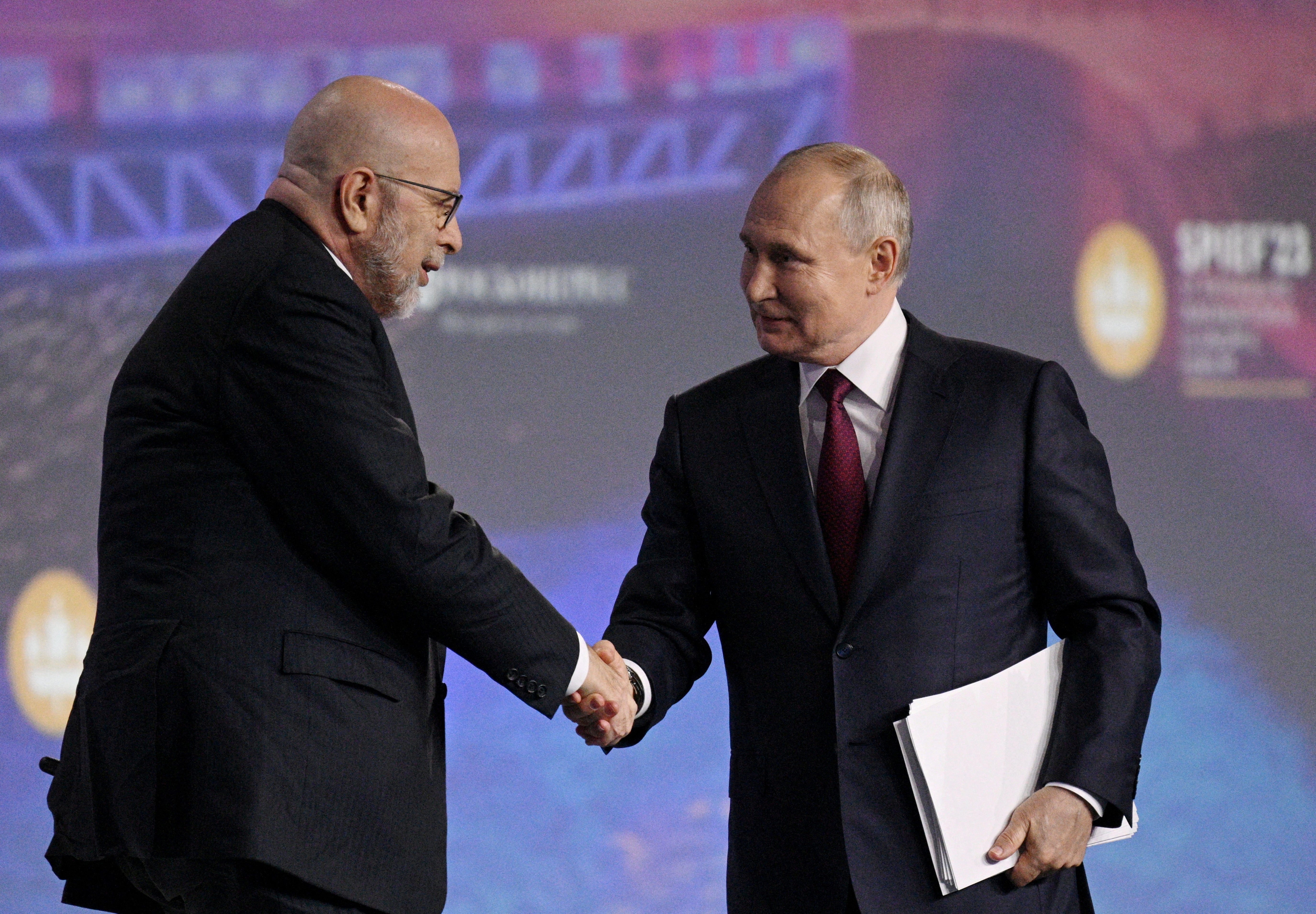 File: ussian President Vladimir Putin shakes hands with moderator Dimitri Simes during a session of the St. Petersburg International Economic Forum