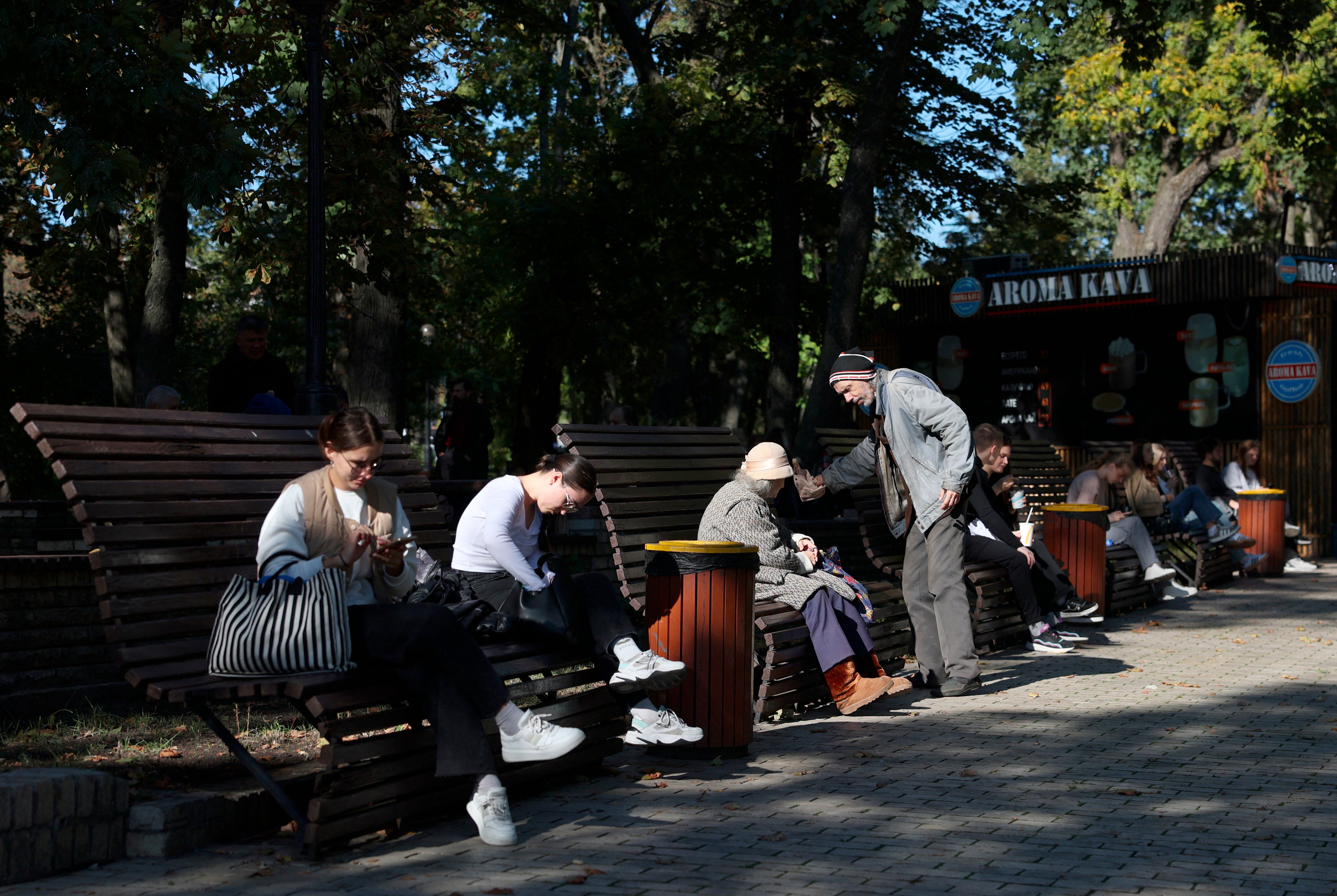 Local residents sit on benches in the park on a sunny autumn day in central Kyiv