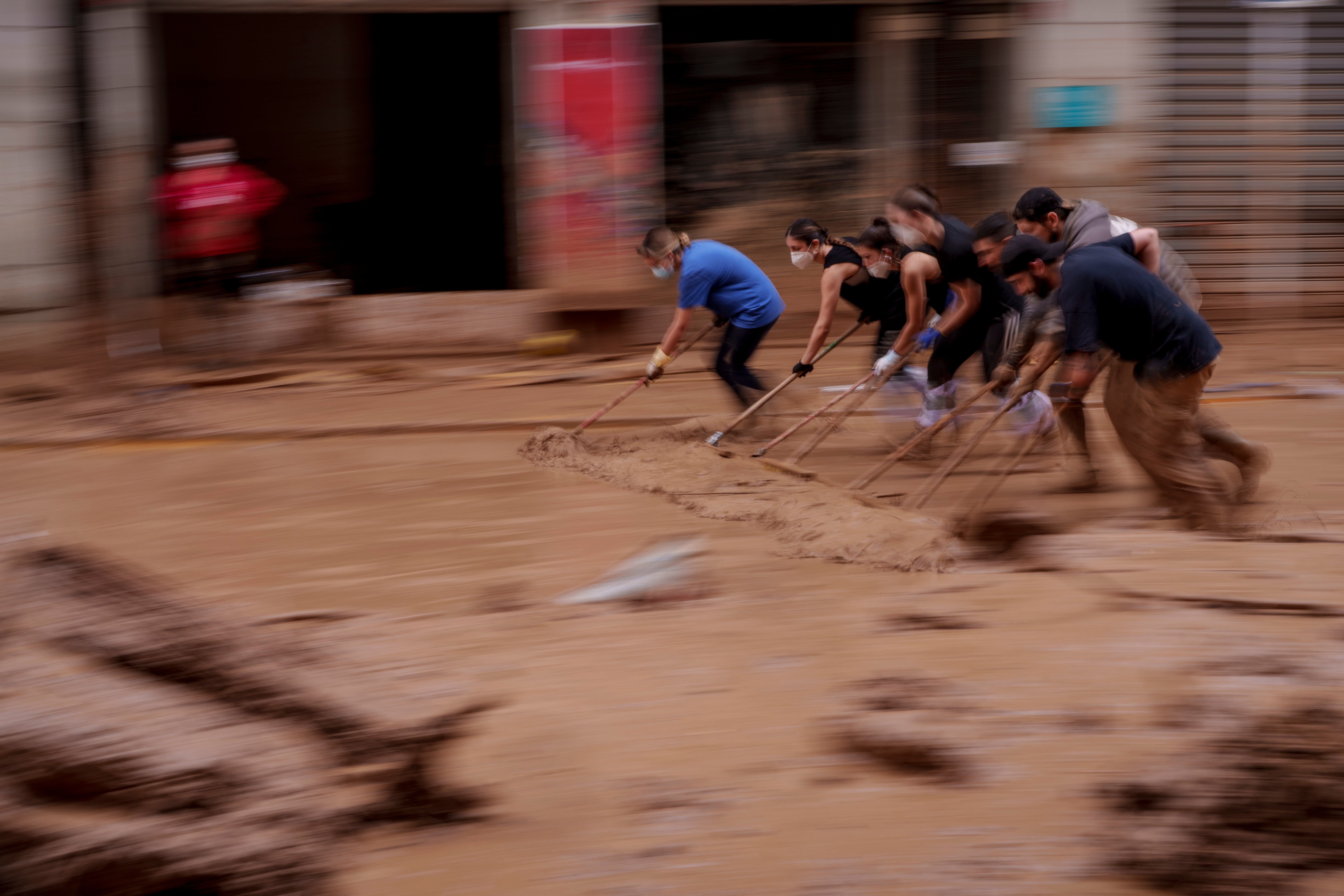 People clear mud from a street in an area affected by floods in Catarroja, Spain