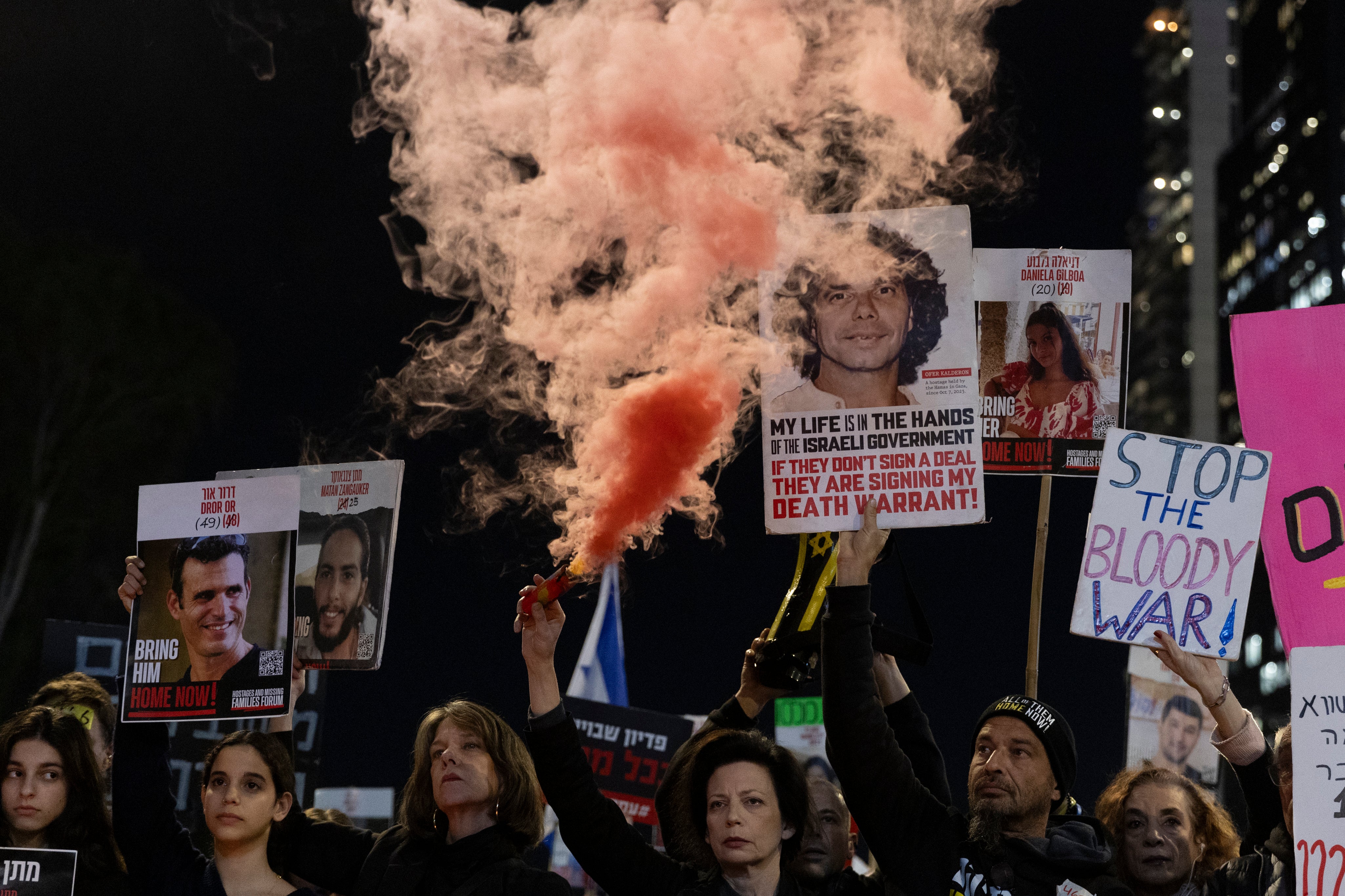 Protesters hold photos of hostages and a smoke torch during a demonstration calling for the return of hostages held by Hamas