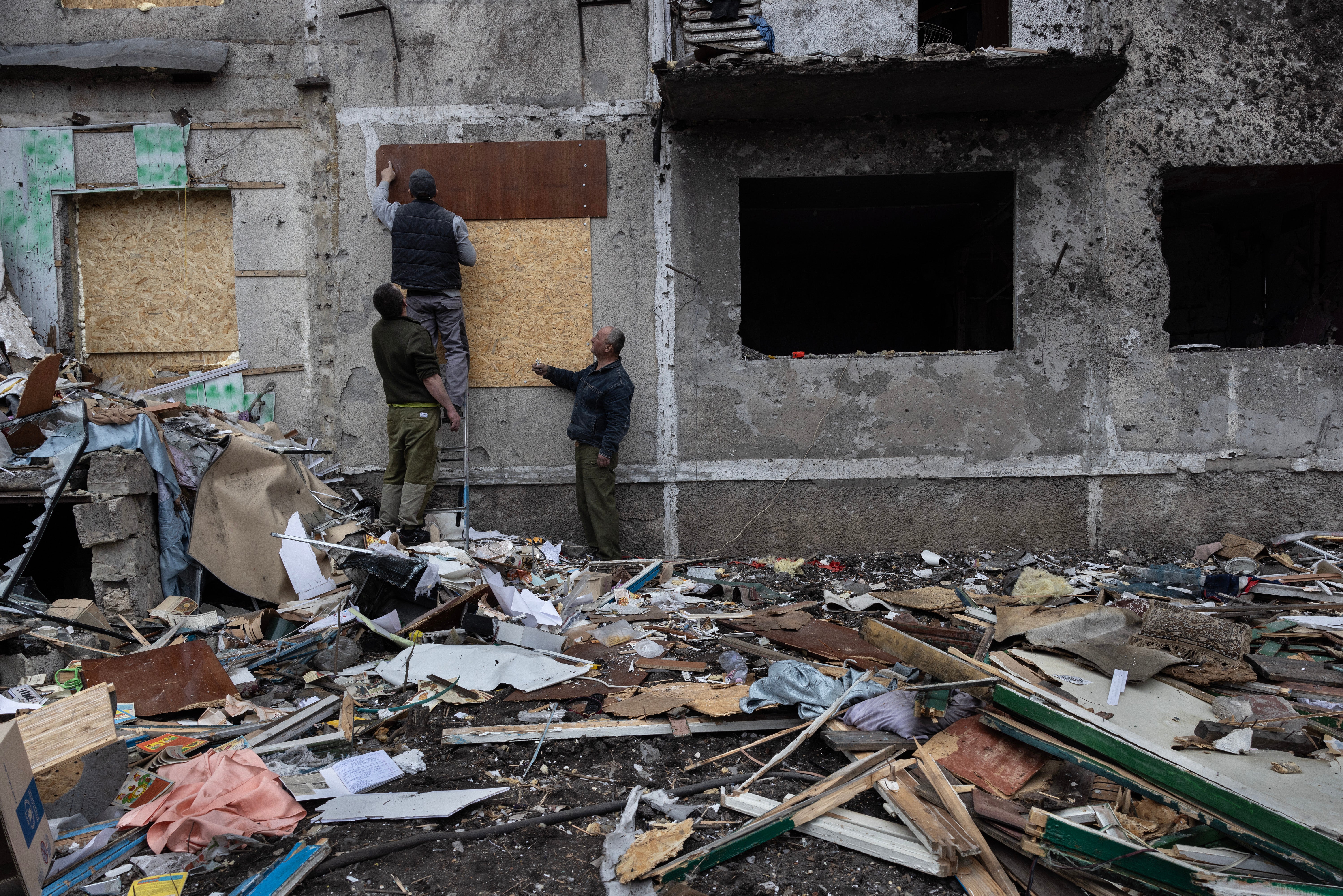 Ukrainian workers clean up debris using particle board to repair broken windows on 10 March 2025.